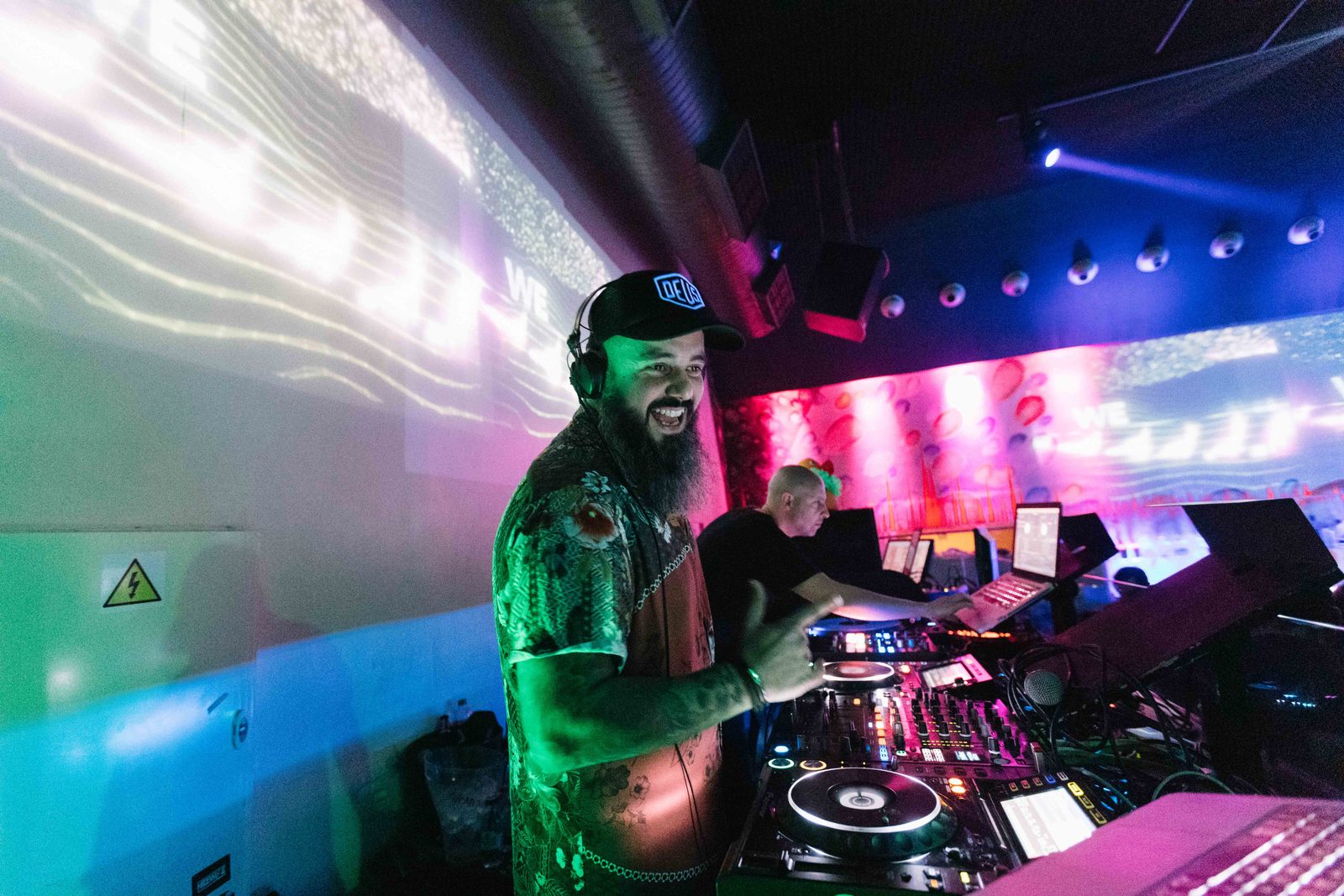 DJ em cabina, com a sala banhada em luz de cor